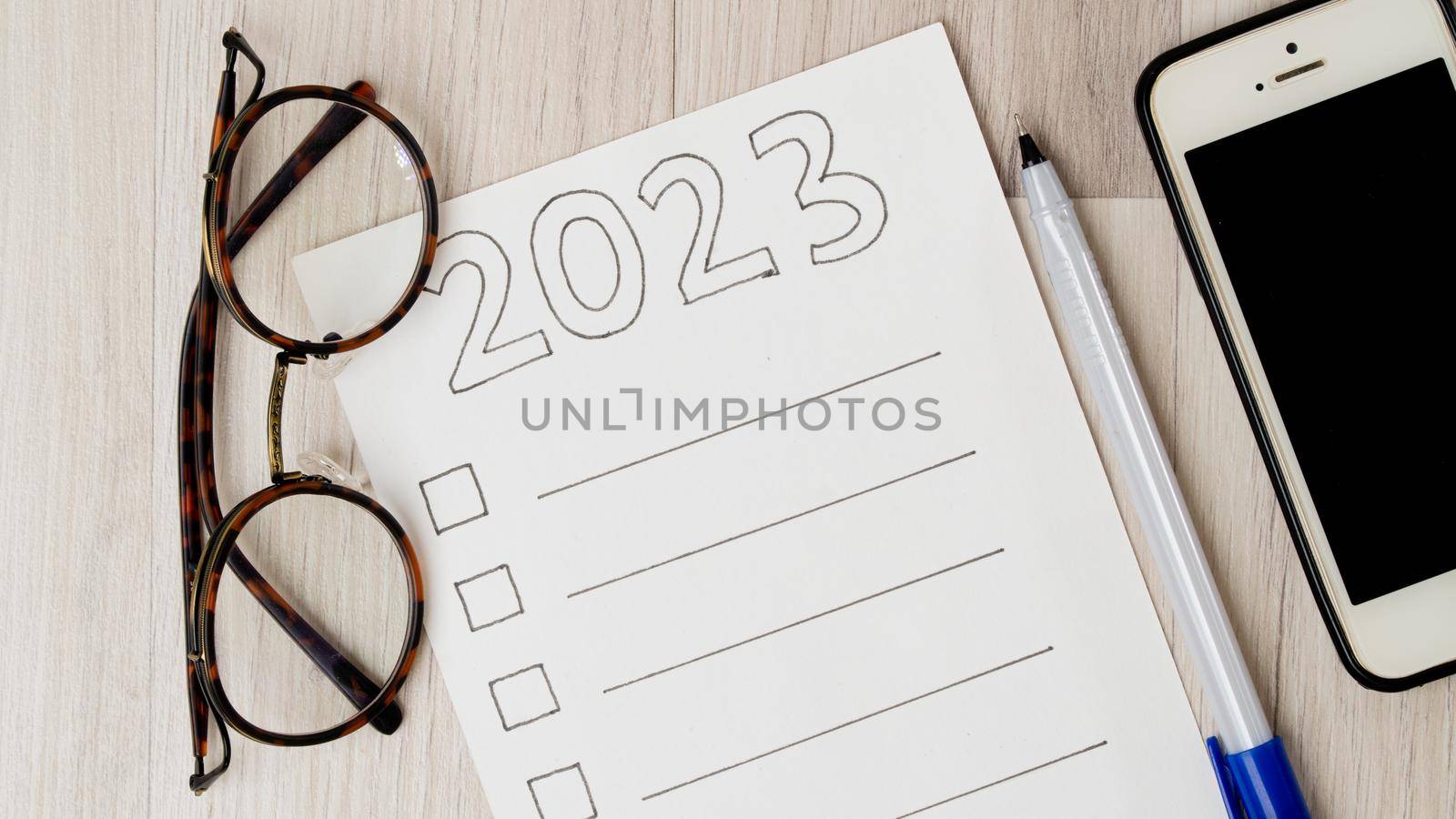 To-do list with squares for ticks and lines for text, glasses, pen and phone on a wooden background. High quality photo