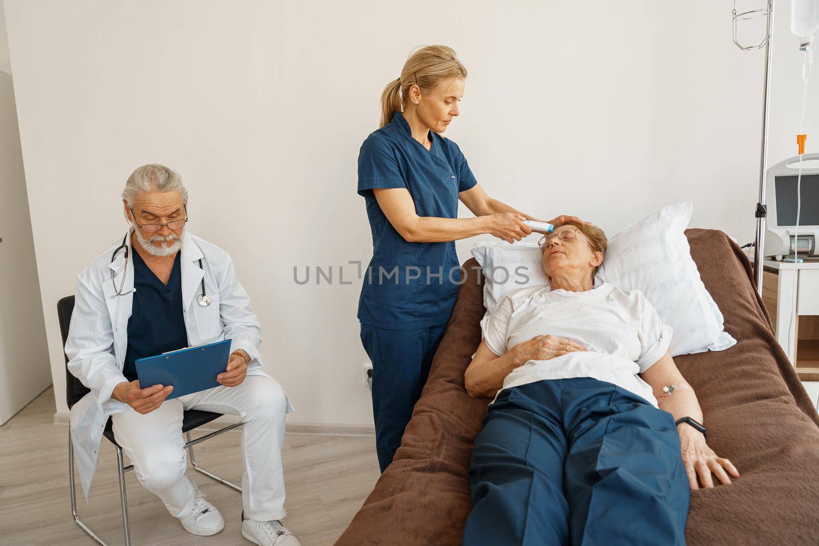 Doctor measures patient's temperature with non-contact thermometer during treatment in hospital ward