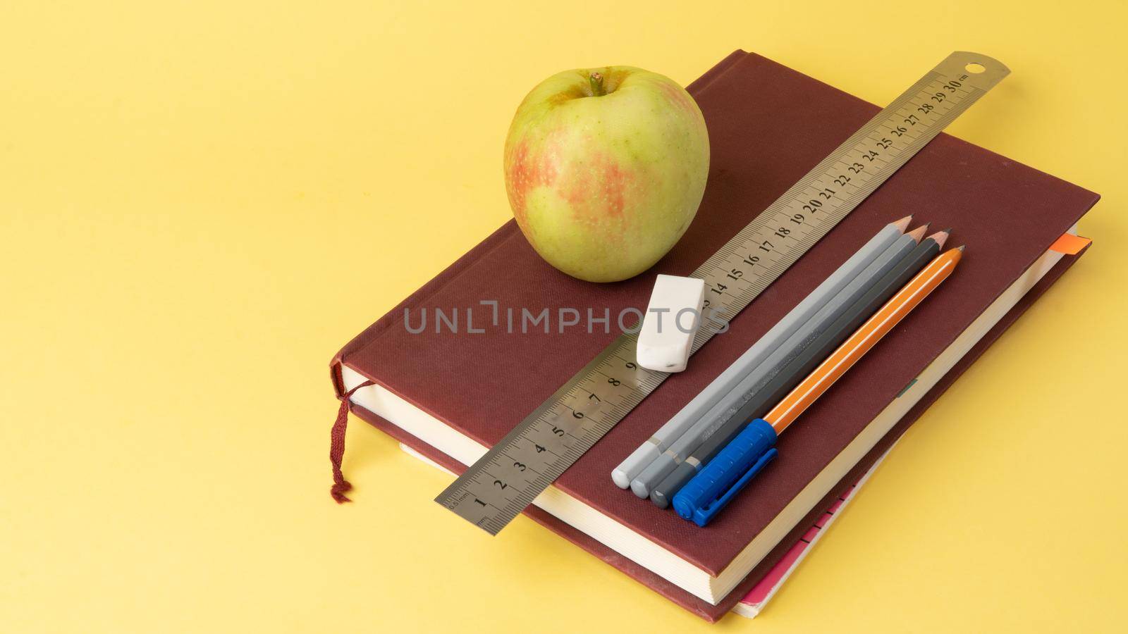 Educational supplies - stationery, book, apple on a yellow background. High quality photo
