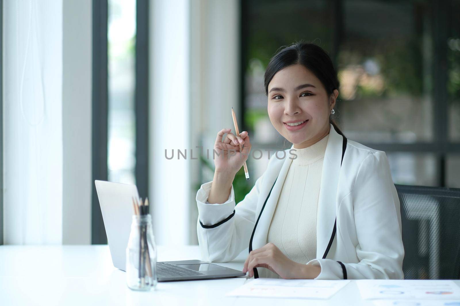 Charming Asian woman working at the office using a laptop Looking at the camera..