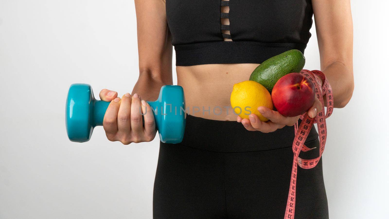 Athletic woman with fruits and vegetables, dumbbells and measuring tape - diet, training, trainer nutritionist. High quality photo