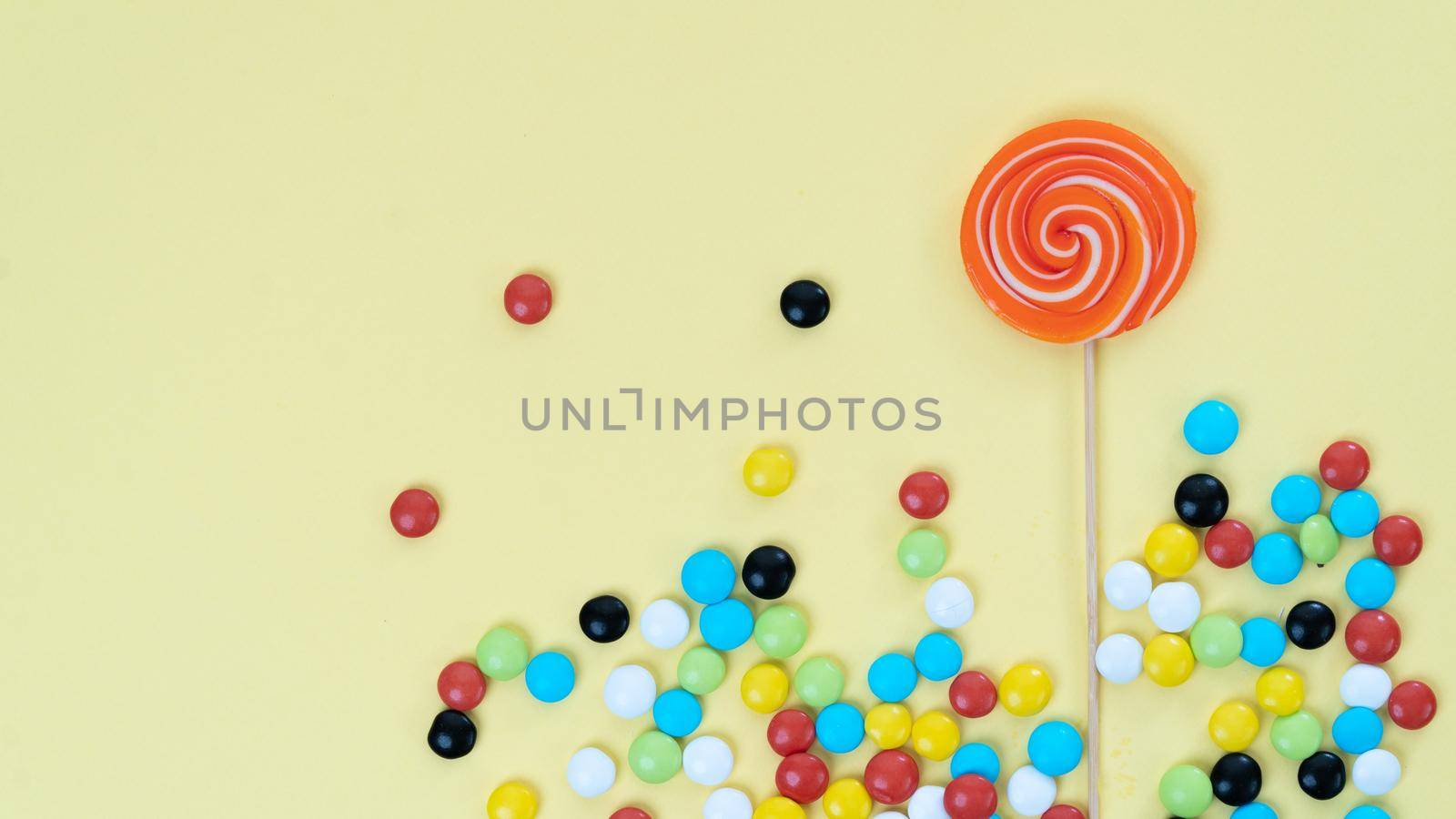 Sweets on a bright colored background - lollipop and multi-colored dragee with space for text by voktybre