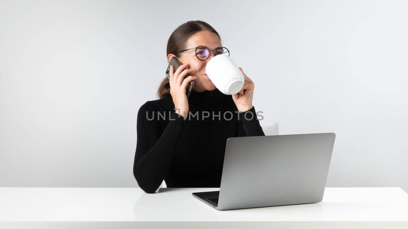 Woman at laptop talking on the phone and drinking coffee - workplace by voktybre