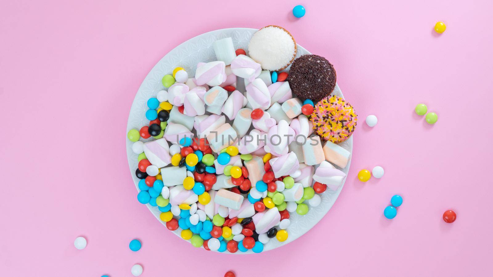 Colorful sweets on a plate on a pink background - sugar food. High quality photo