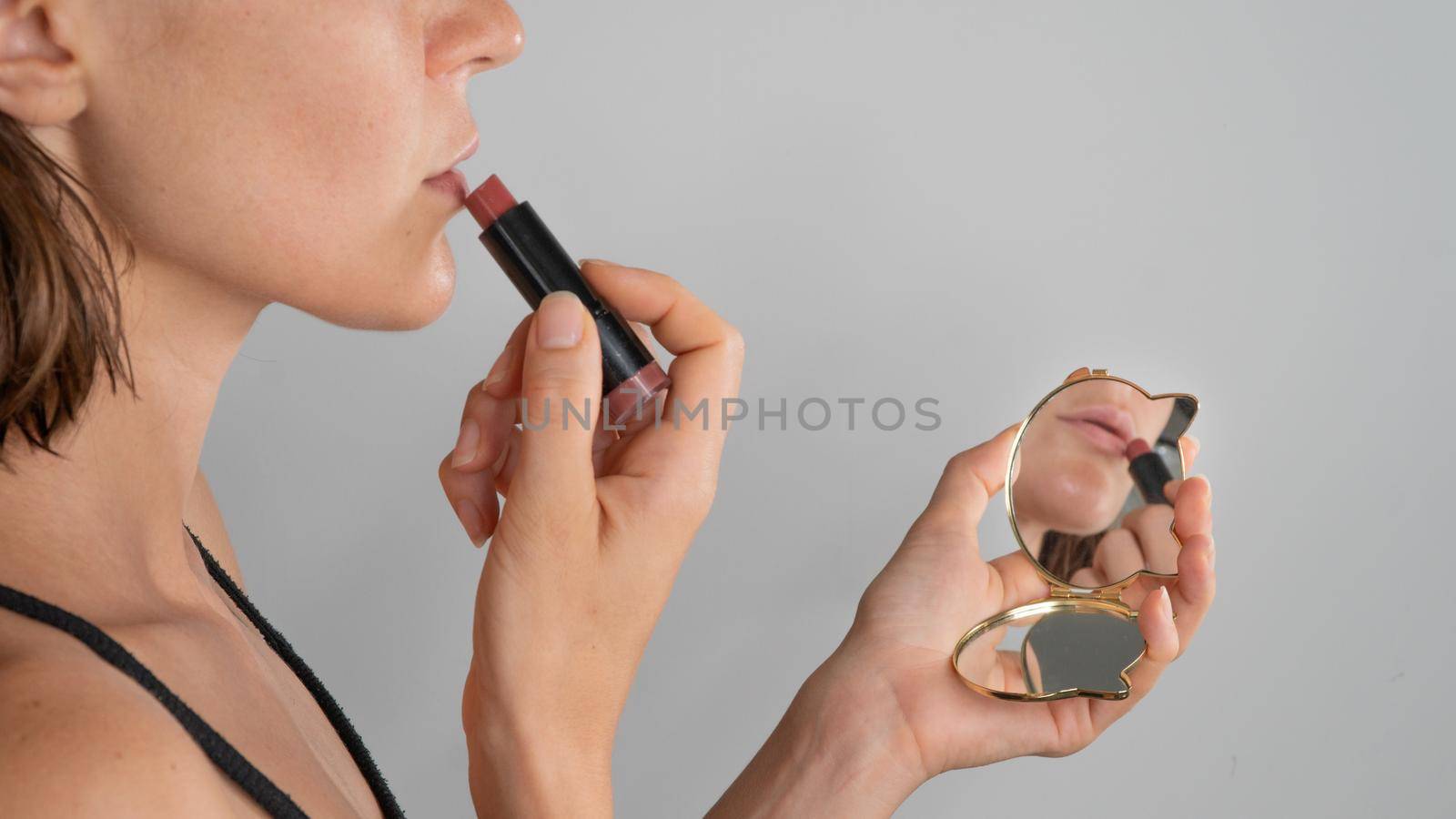 The girl paints her lips with lipstick in a pocket mirror, reflection - makeup. High quality photo