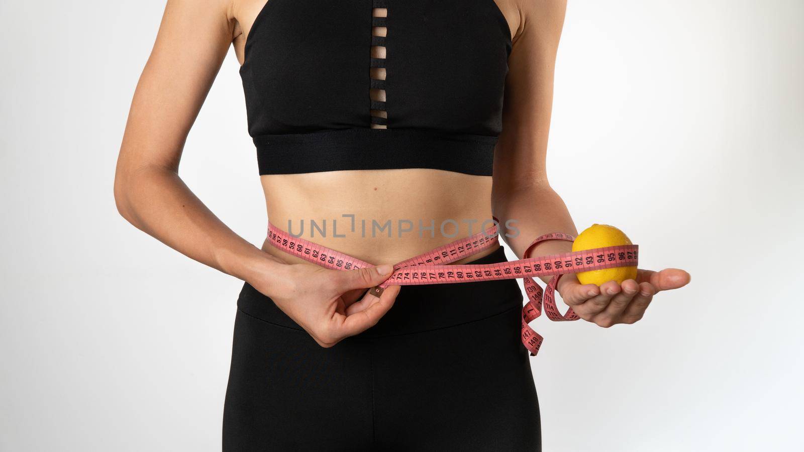 A woman measures the figure with a ribbon, a lemon in her hand - weight loss, healthy eating and sports. High quality photo