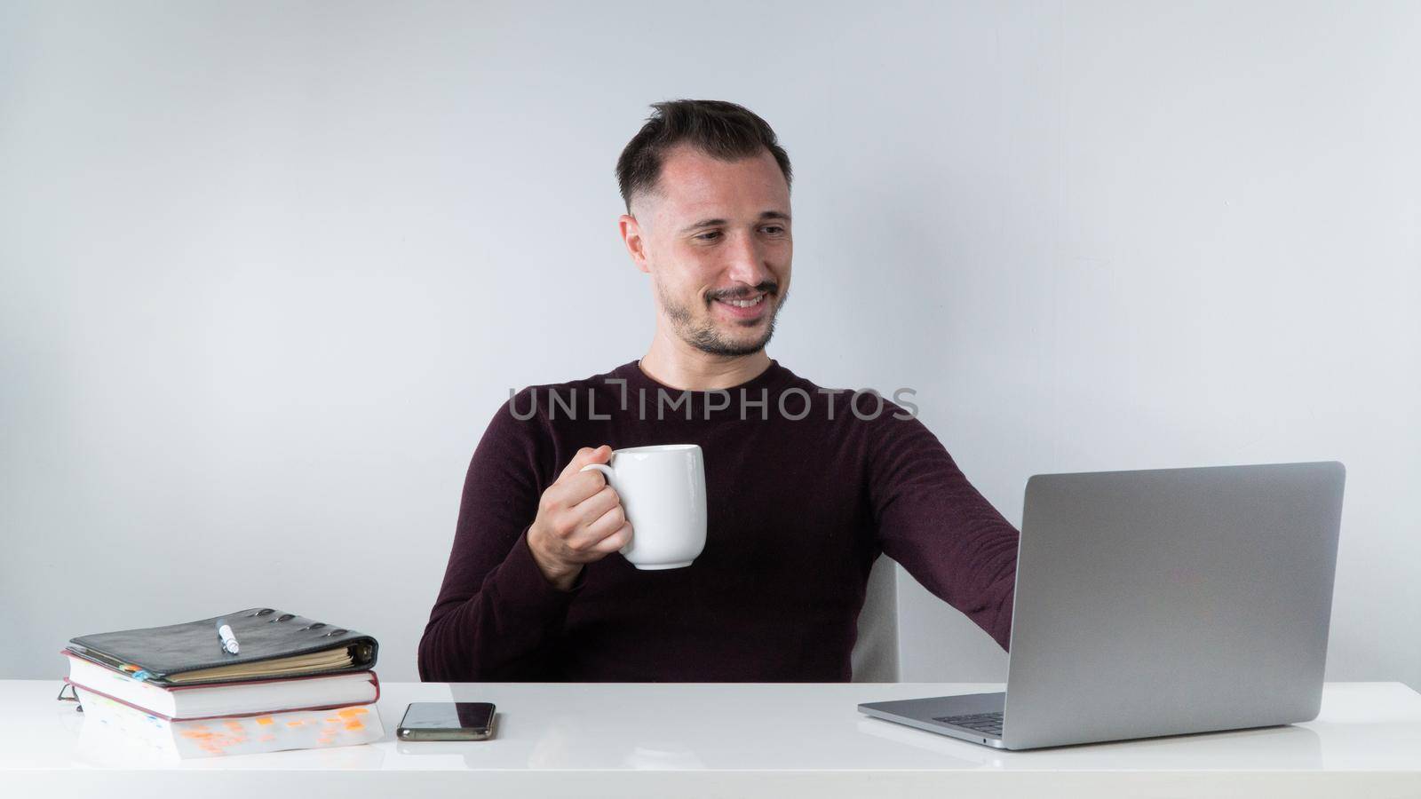 An employee negotiates a video connection in a laptop with a mug of coffee, work in the office or freelance at home by voktybre