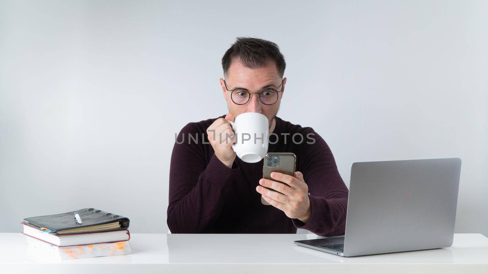 A man at work drinks coffee and looks at the phone screen in surprise with big eyes - unexpected news by voktybre