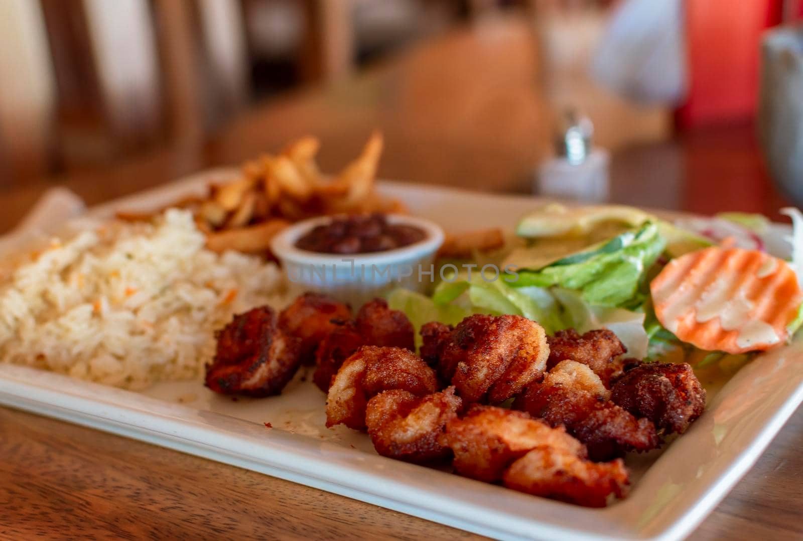 Breaded shrimp with rice and salad served on wooden table. Close up of breaded shrimp with french fries and salad served on wooden table. Seafood food concept served on the table