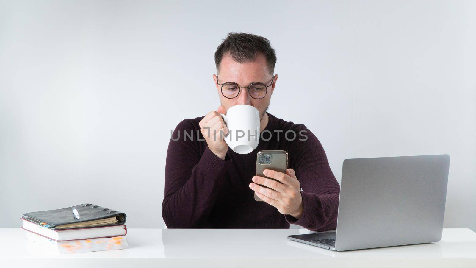 A man at work drinks coffee and looks at a smartphone. High quality photo