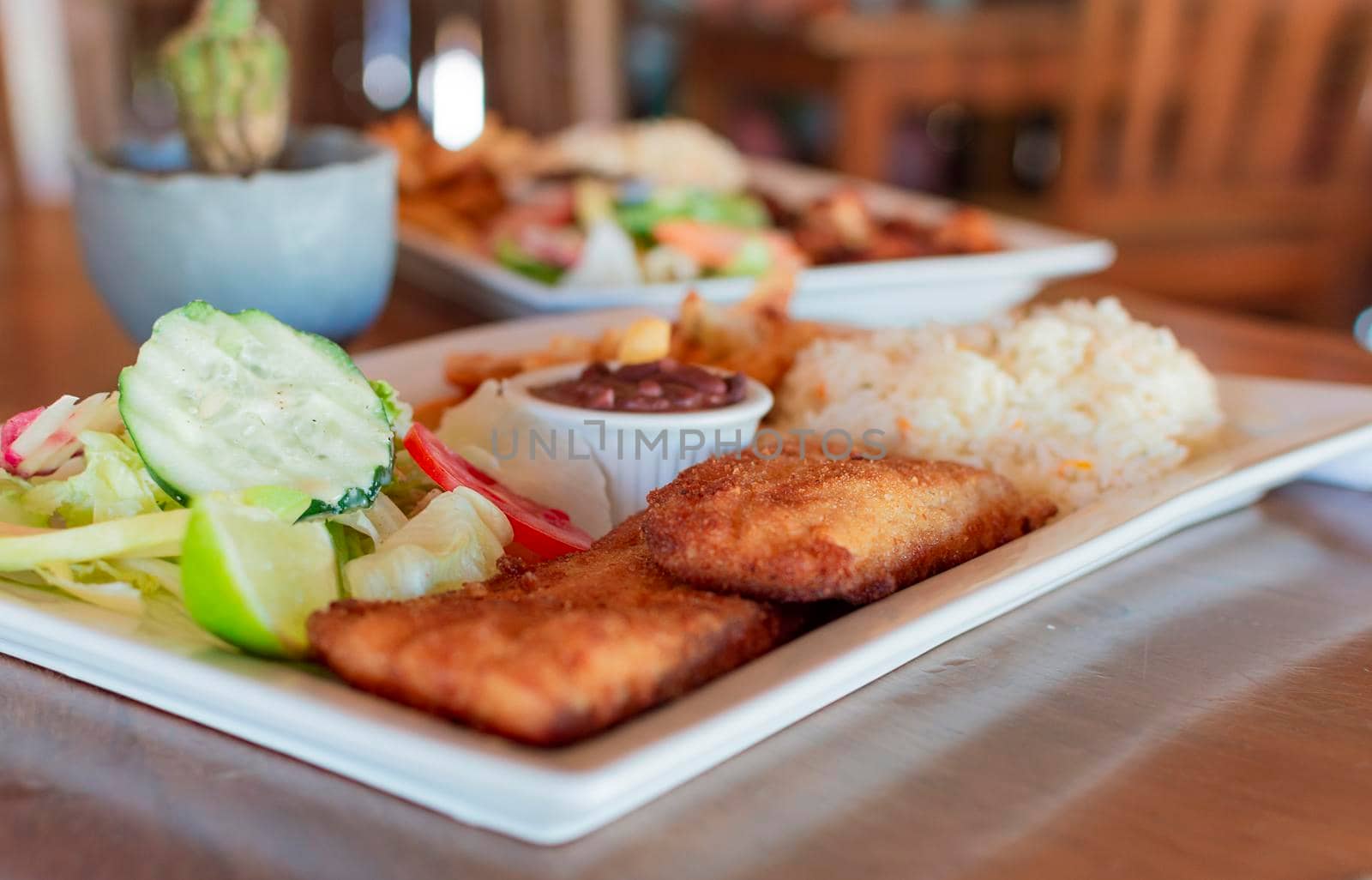 Close up of fried fish fillet with rice and salad served on table with copy space. Gourmet food fried fish fillet with salad rice served on wooden table, gourmet food fried fish fillet