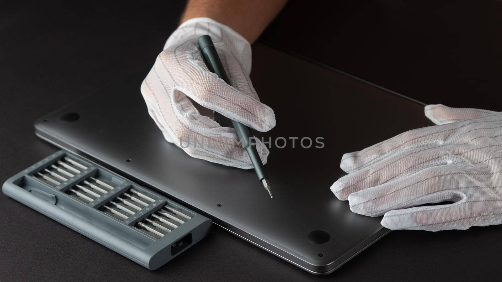 The master repairs a laptop in white gloves with a screwdriver and a set of bits. High quality photo