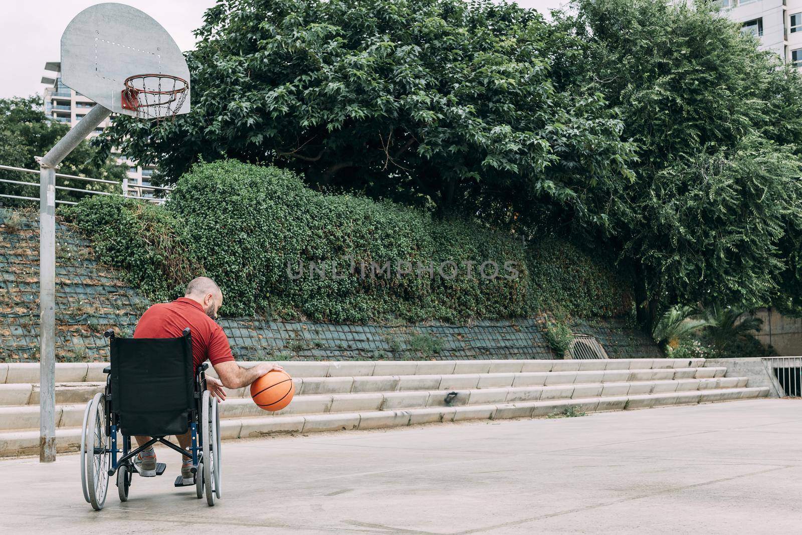 disabled man in wheelchair playing on basket on the basketball court alone, concept of adaptive sports and physical activity, rehabilitation for people with physical disabilities