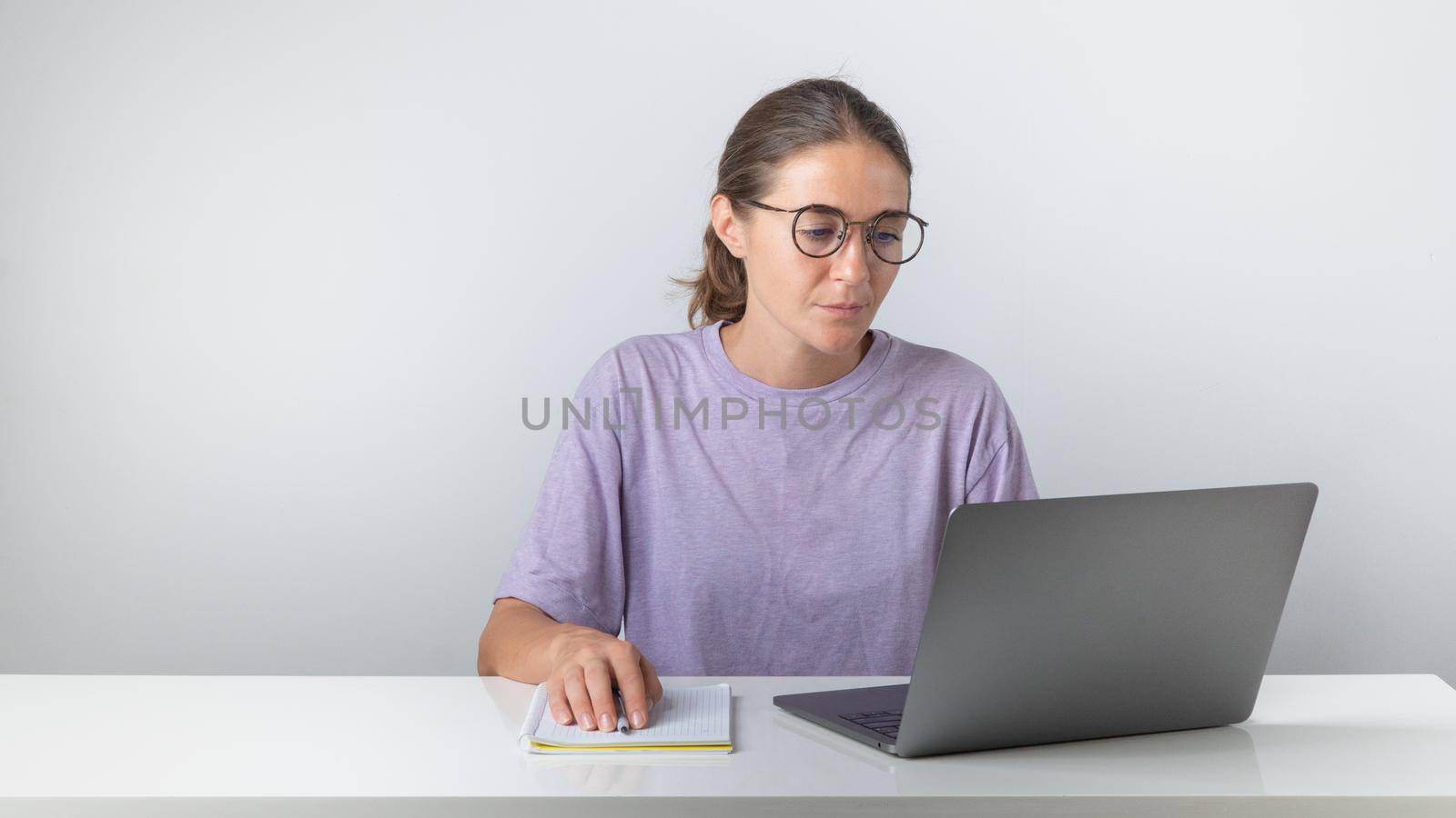 A female student sits at a laptop with a notebook and a pen. High quality photo