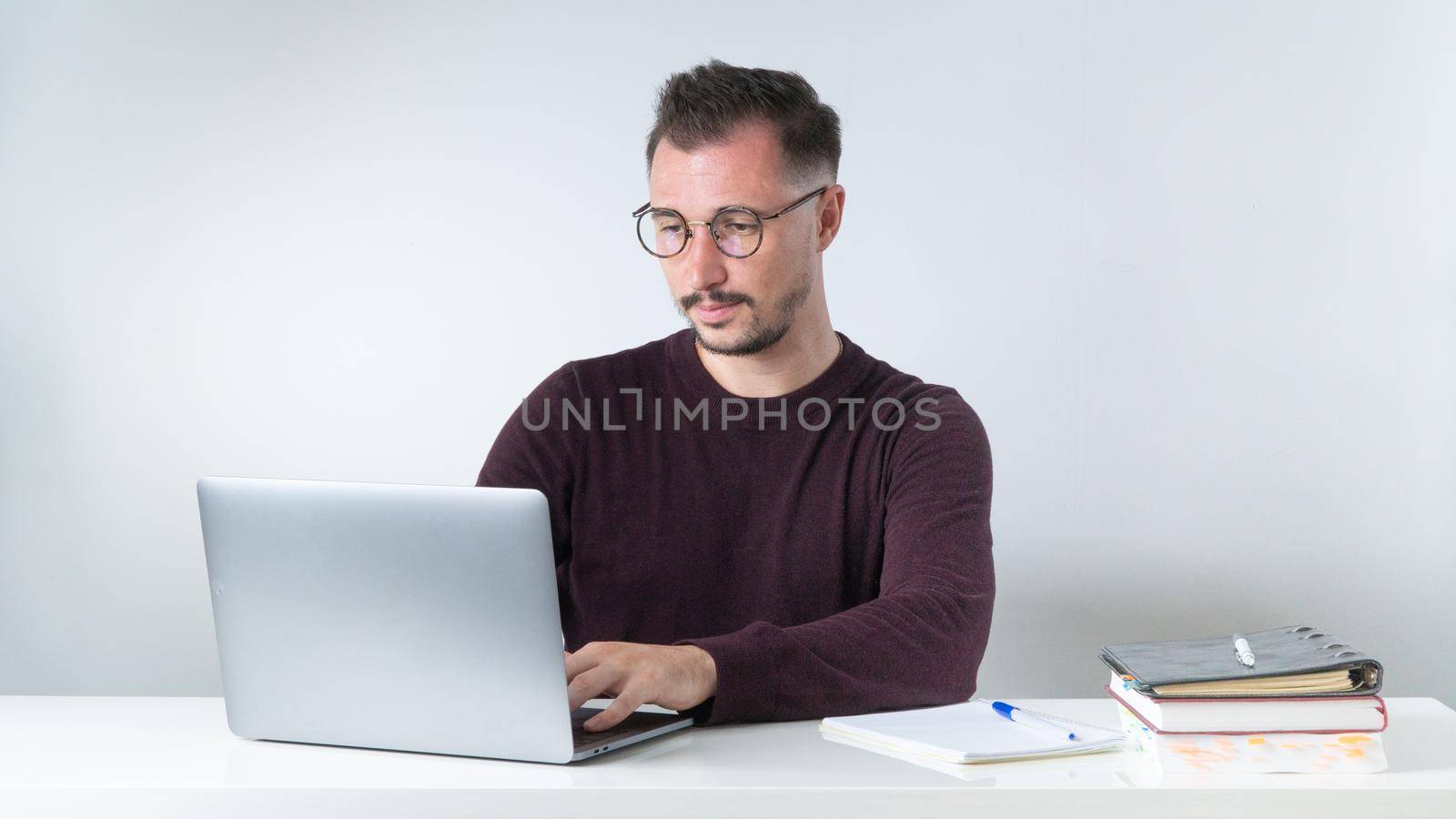 A man with glasses works in the office on a laptop, typing by voktybre