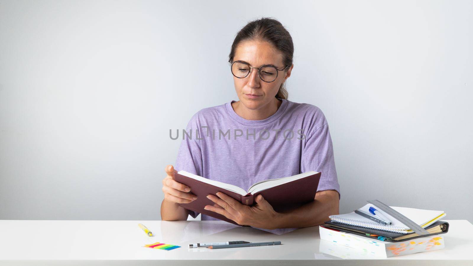 A student girl reads a book at a study table with notebooks and pens. High quality photo