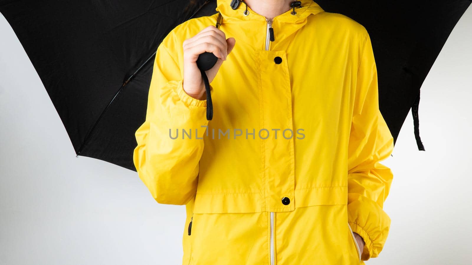 A woman in a yellow raincoat holds a black umbrella on a white background. High quality photo