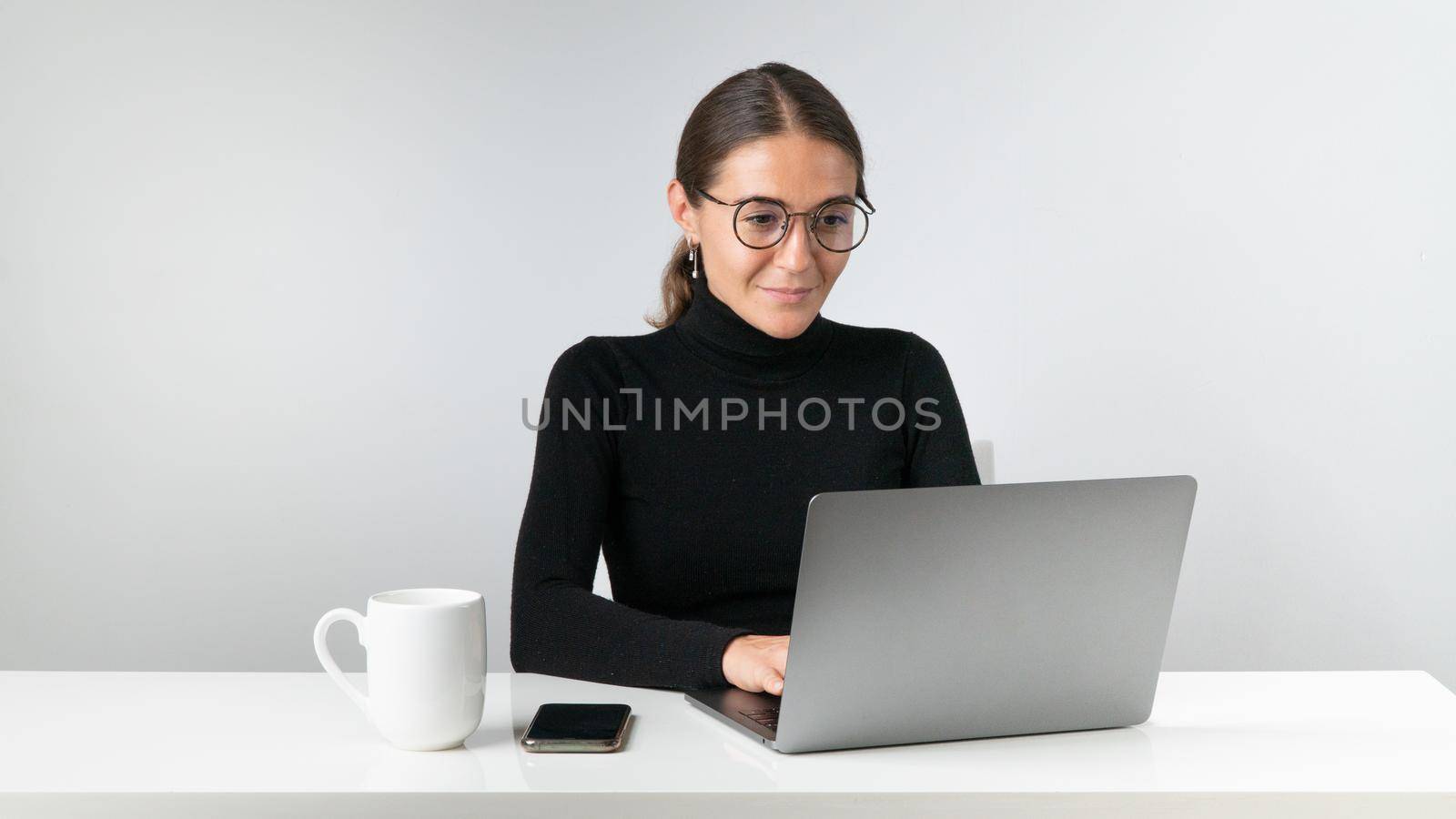 A woman works, studies or communicates at a laptop at a table with a cup and a phone by voktybre