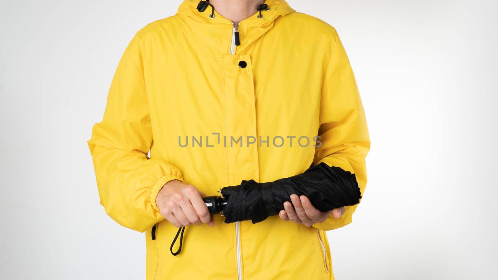 A woman in a yellow raincoat holds a black umbrella on a white background. High quality photo