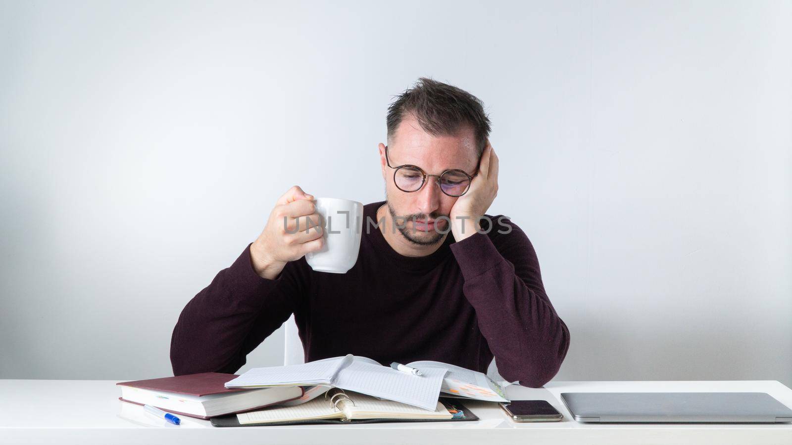 A tired employee is a man with a cup of coffee over a pile of papers. High quality photo