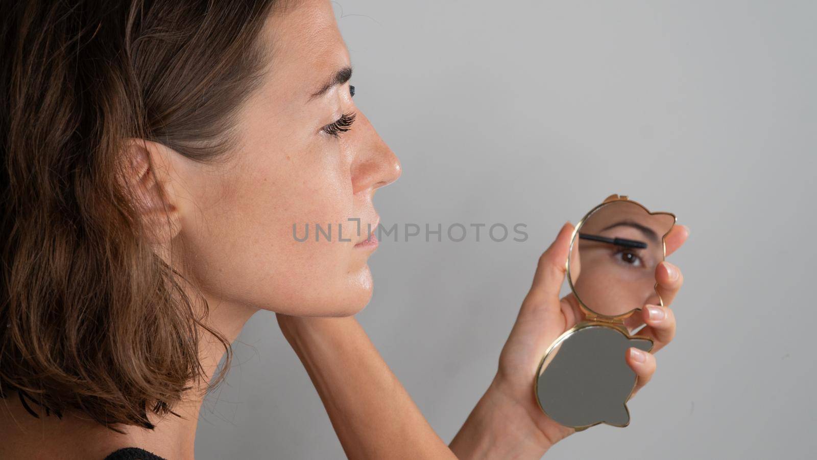 A woman dyes her eyelashes with mascara in a small mirror, a reflection by voktybre