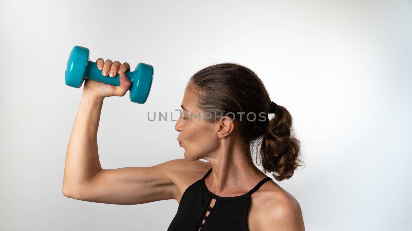 A woman kisses her biceps after a sports workout with a dumbbell in her hands by voktybre