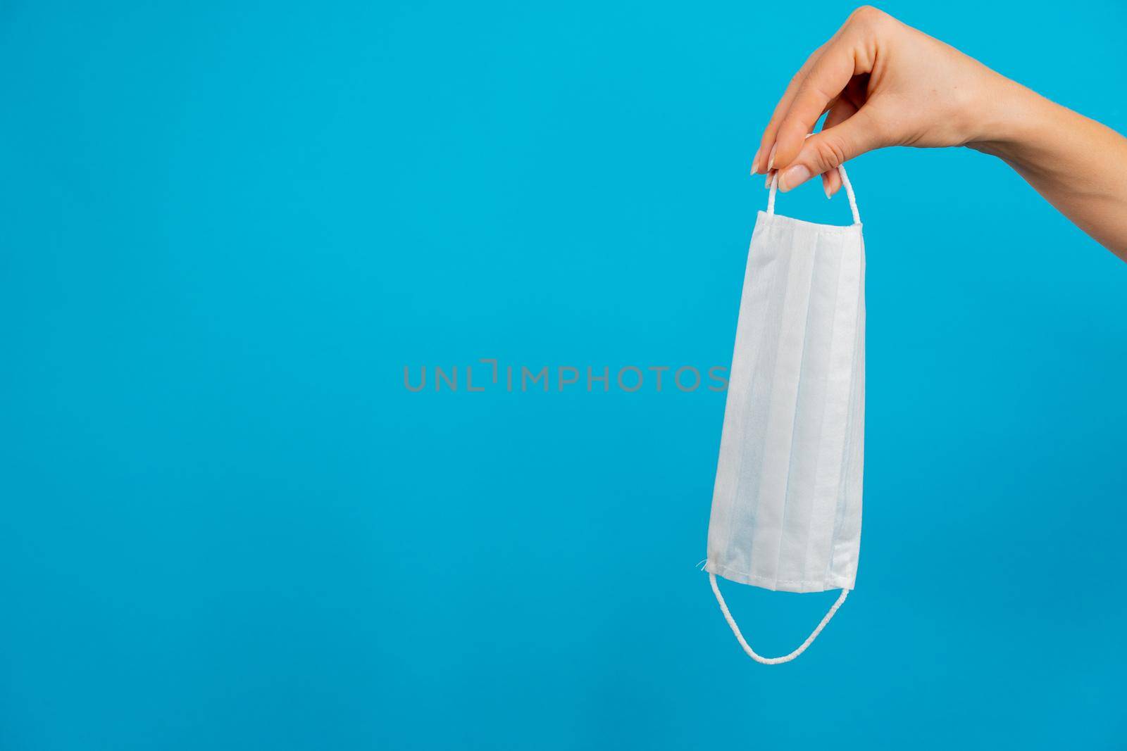 A woman's hand holds a white mask on a blue background, space for text. High quality photo