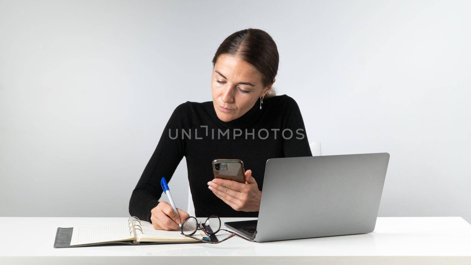 A woman works at a laptop, makes notes in a notebook, planning, routine by voktybre