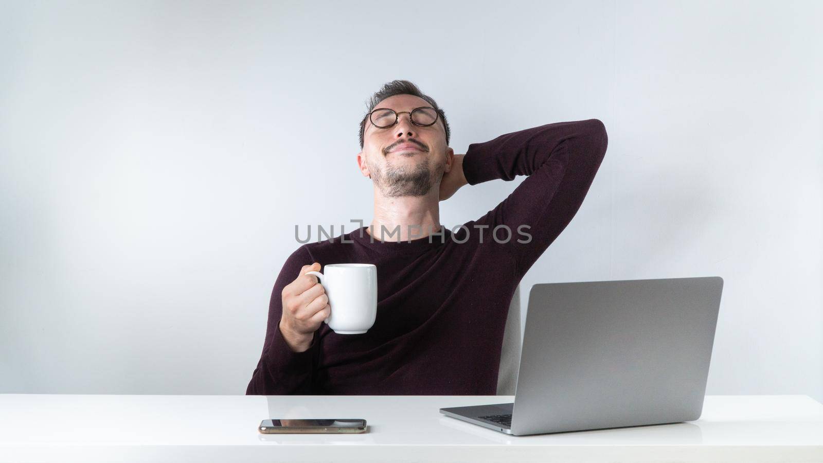 The male employee did a good job - he leaned back in his chair with a cup of coffee or tea. High quality photo