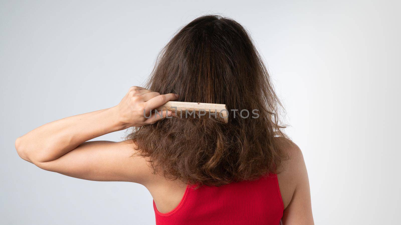 A woman tries to comb her tangled hair from behind with a comb - hair problems by voktybre