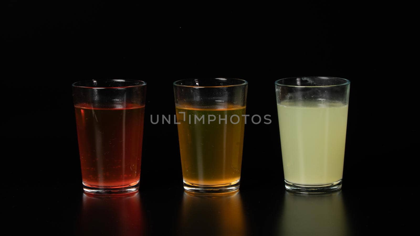 Three glasses of colored water, drinks, juices and cocktails on a black background by voktybre