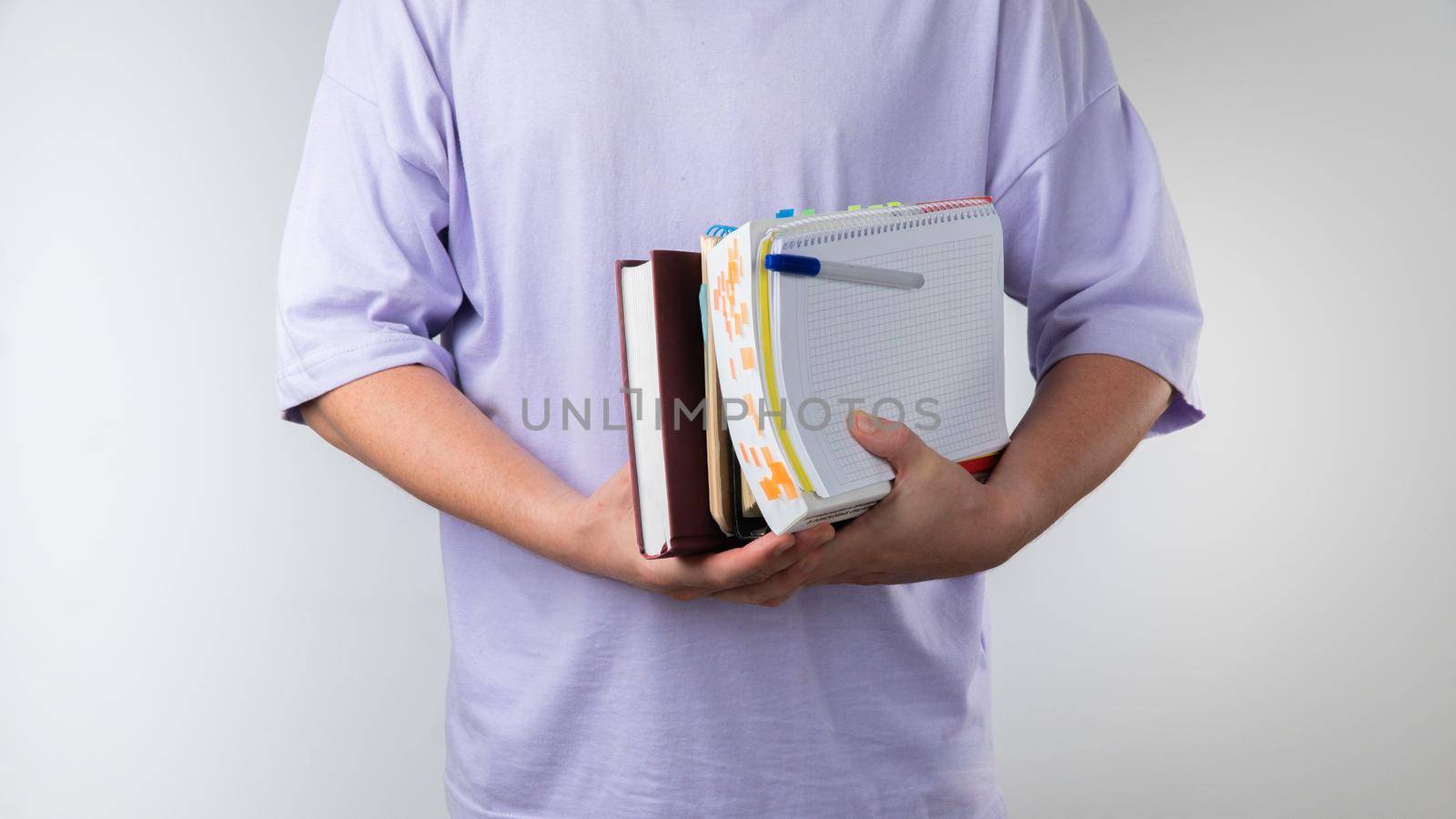A student with textbooks and notebooks in his hands goes to class close-up on a white background by voktybre