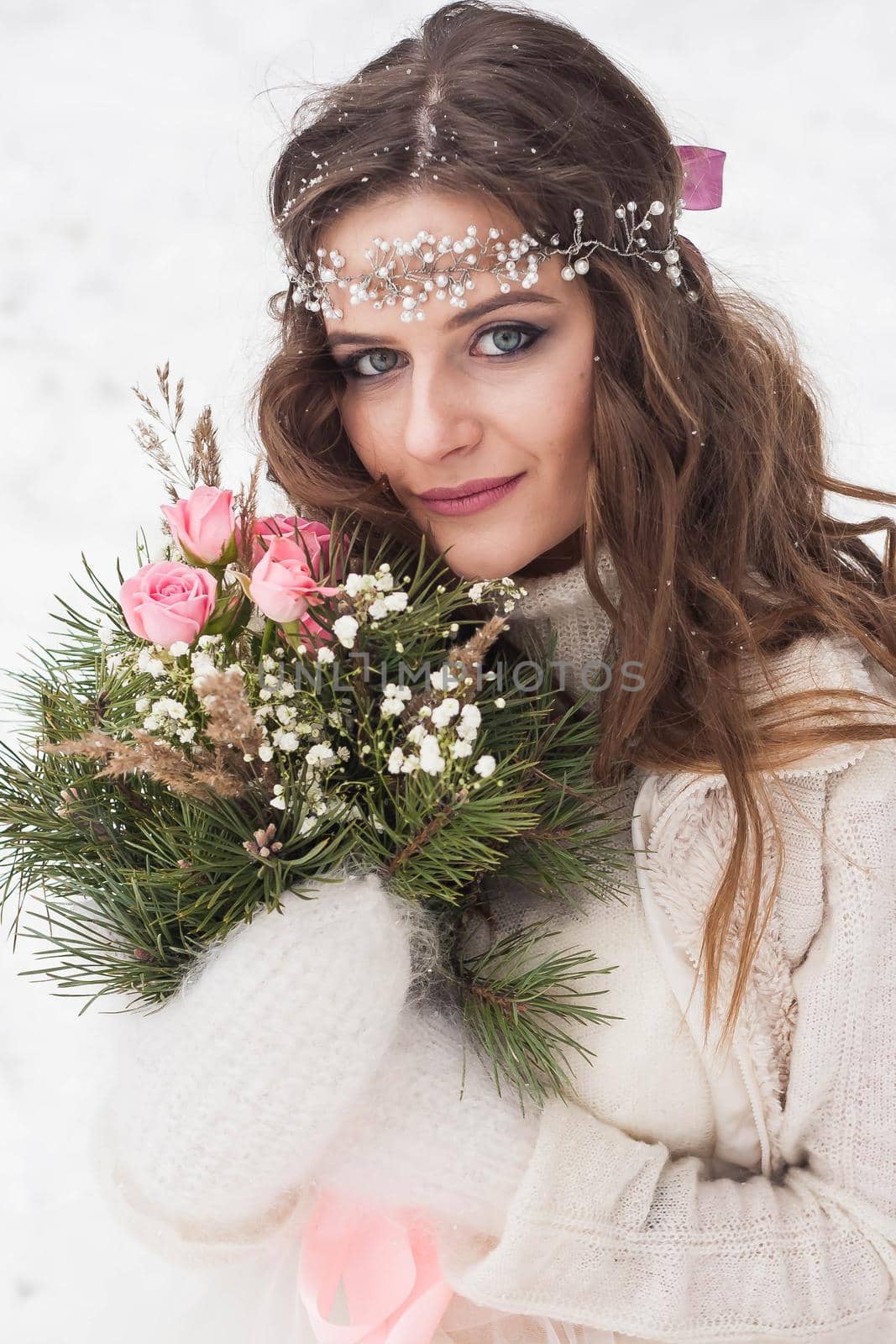 Beautiful bride in a white dress with a bouquet in a snow-covered winter forest. Portrait of the bride in nature.