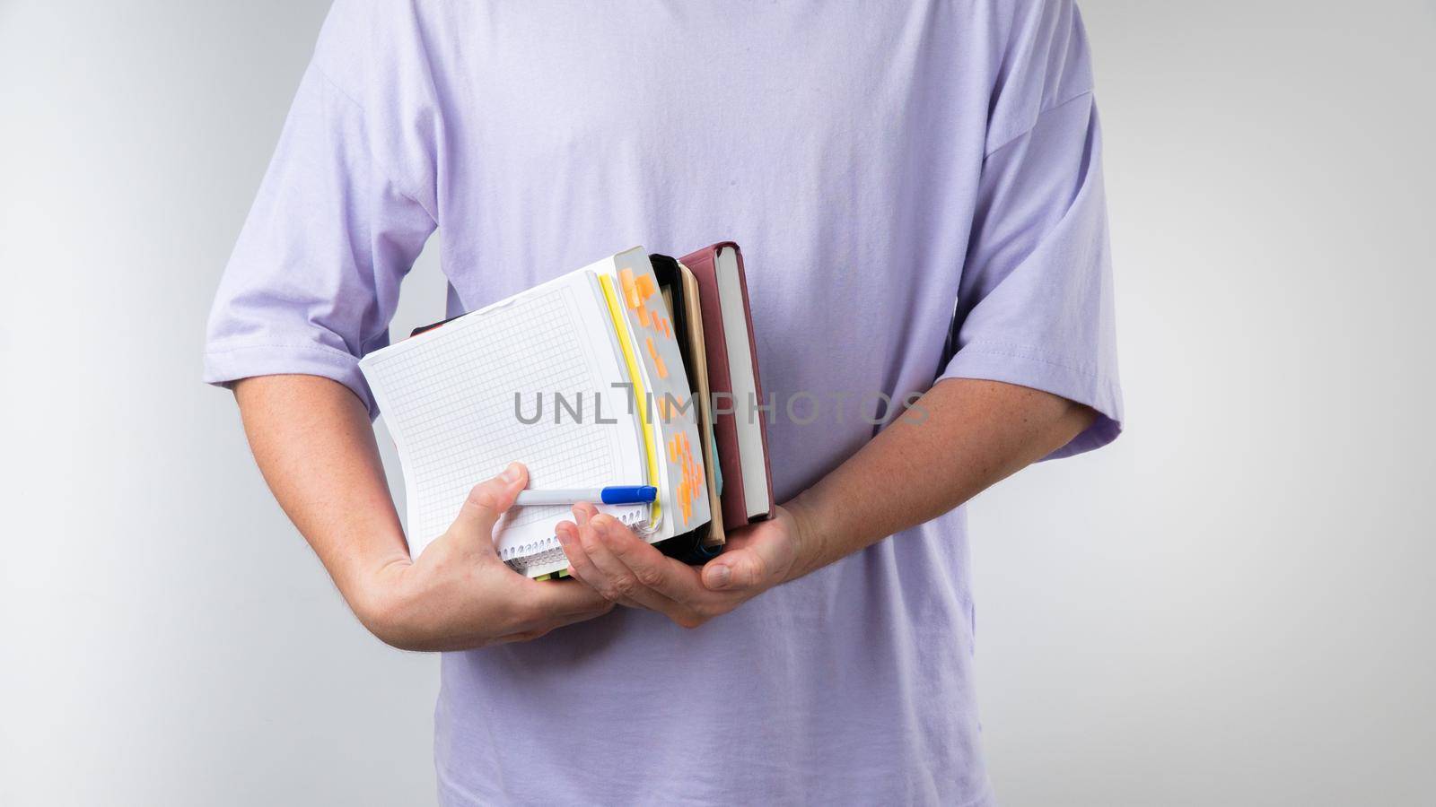 Male student holds textbooks and notebooks for classes in an educational institution with his armpit. High quality photo