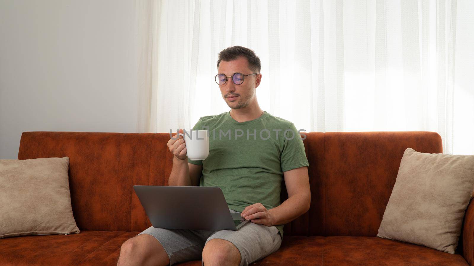 A man with a laptop sits on the couch at home and drinks coffee. High quality photo