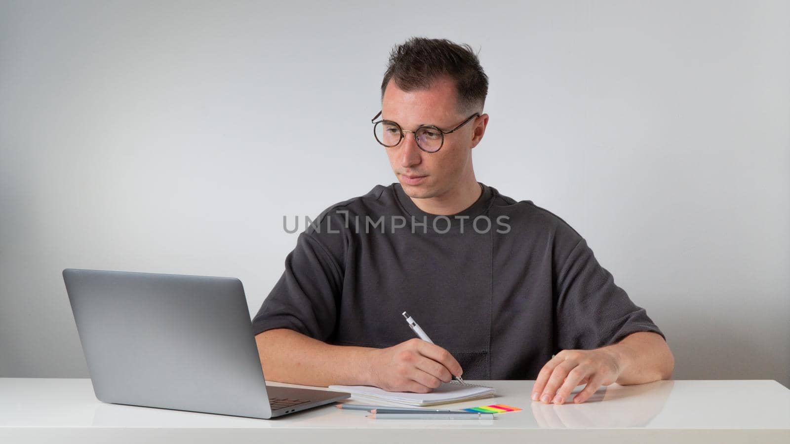 A guy at a laptop makes notes in a notebook at the workplace - work and study. High quality photo