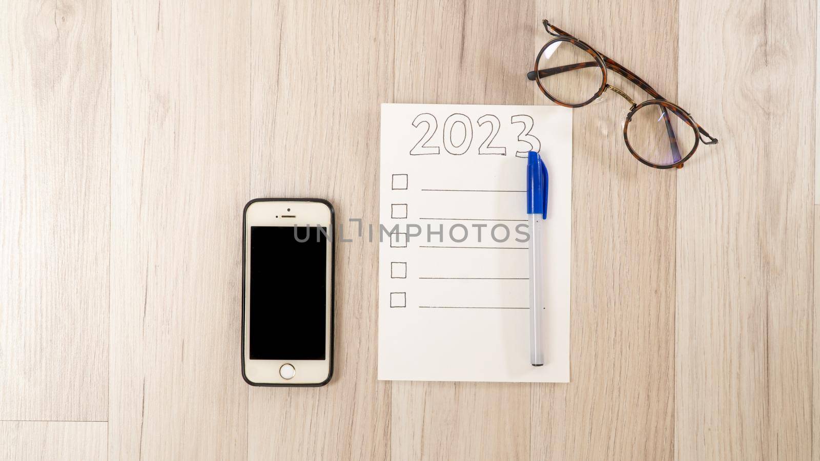 Checklist for 2023, smartphone and glasses on a wooden table, to-do list for the new year by voktybre