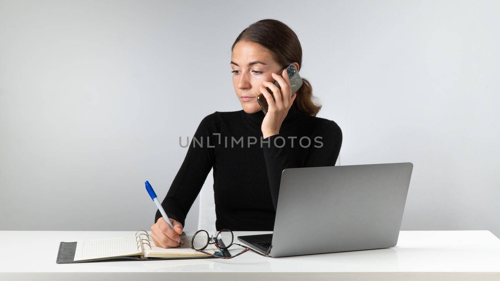 A phone call at the workplace - a woman at a laptop with a phone in the office. High quality photo