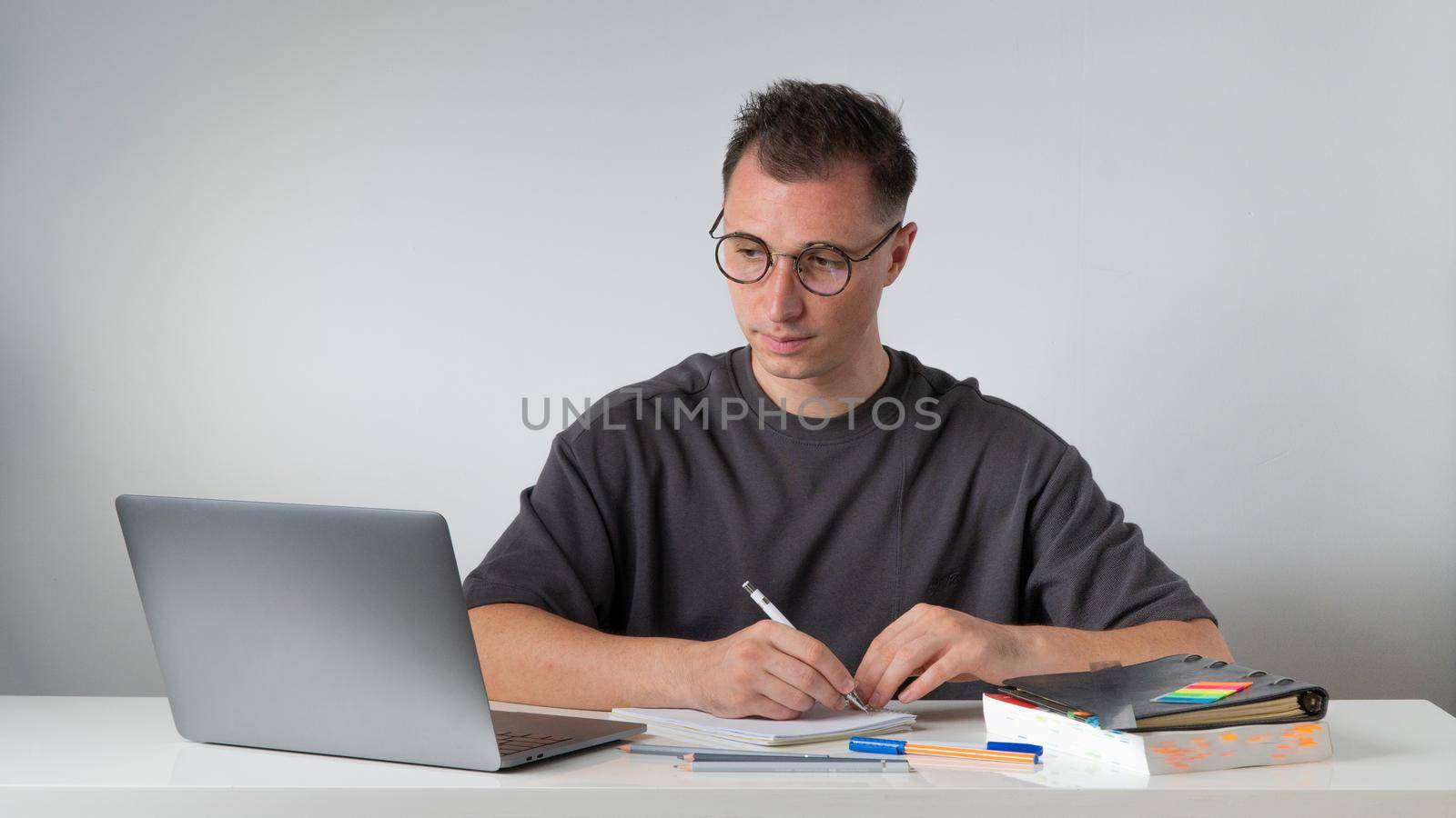 A man at his desk writes in a notebook, looks at a laptop. High quality photo