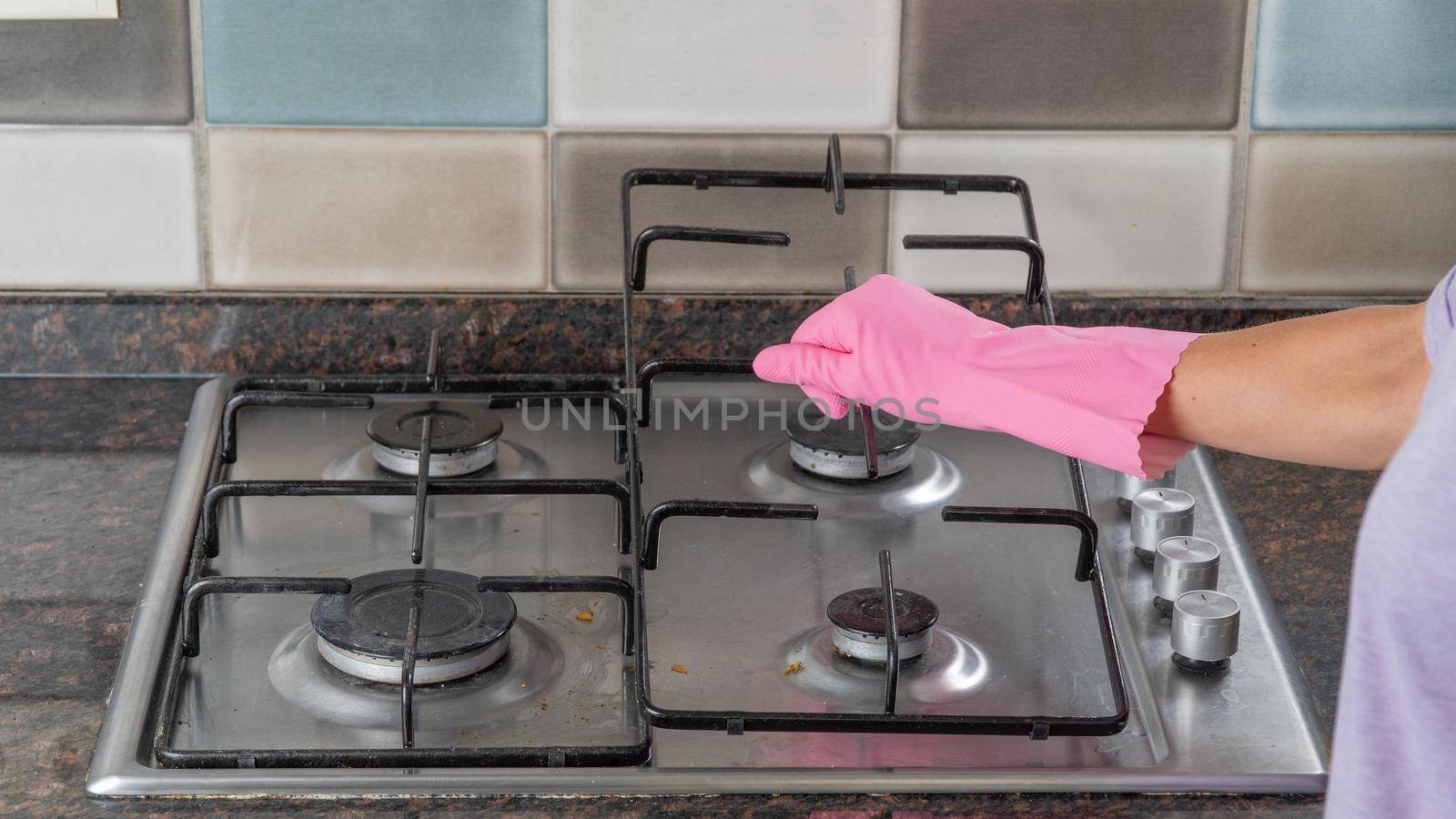 A woman's hand in a rubber glove holds the grate from the gas stove to wash the surface