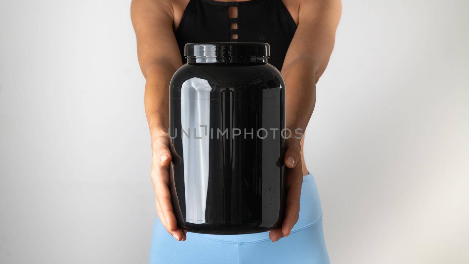Women's hands hold a large can of sports nutrition, useful supplements for training. High quality photo