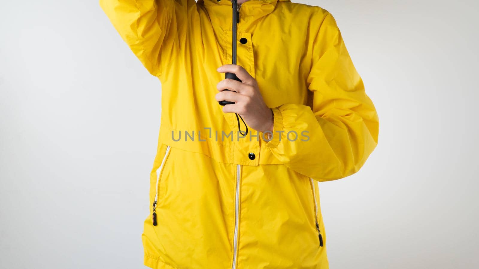 A woman in a yellow raincoat holds a black umbrella on a white background. High quality photo