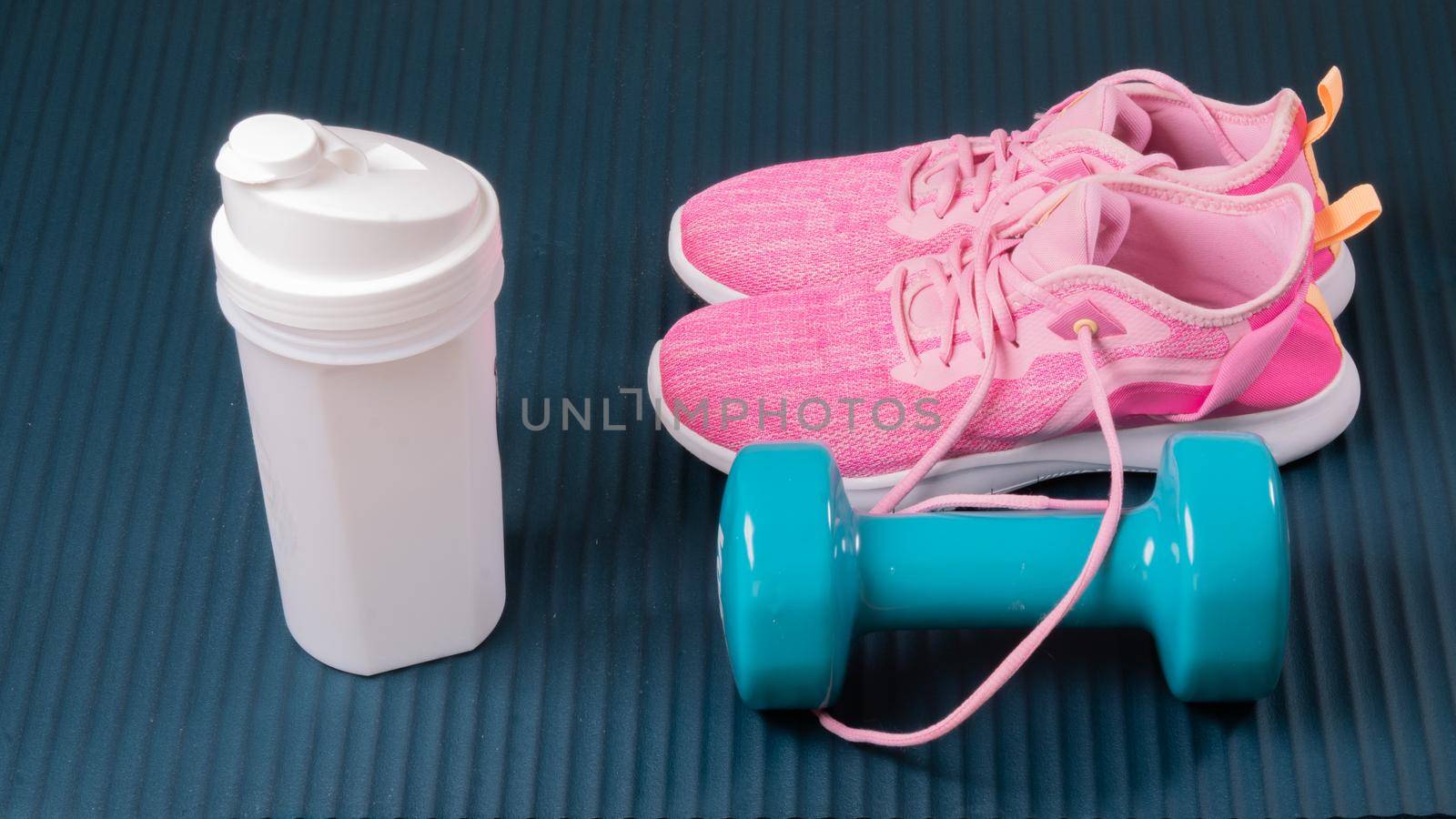 Sneakers, dumbbell and shaker on the mat for training sports background. High quality photo
