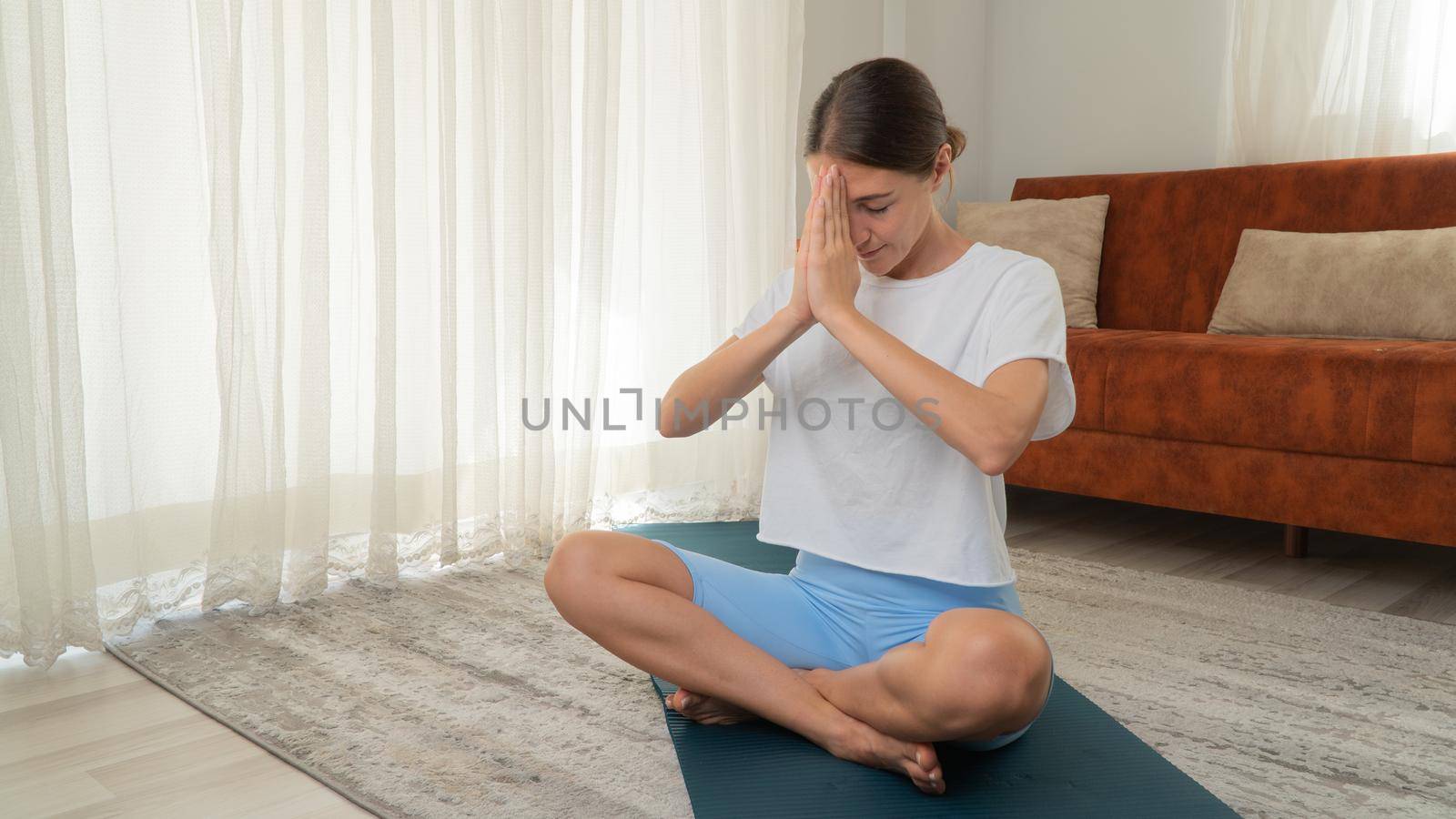 A woman meditates in the lotus position on the floor and makes namaste from the palms of her hands by voktybre