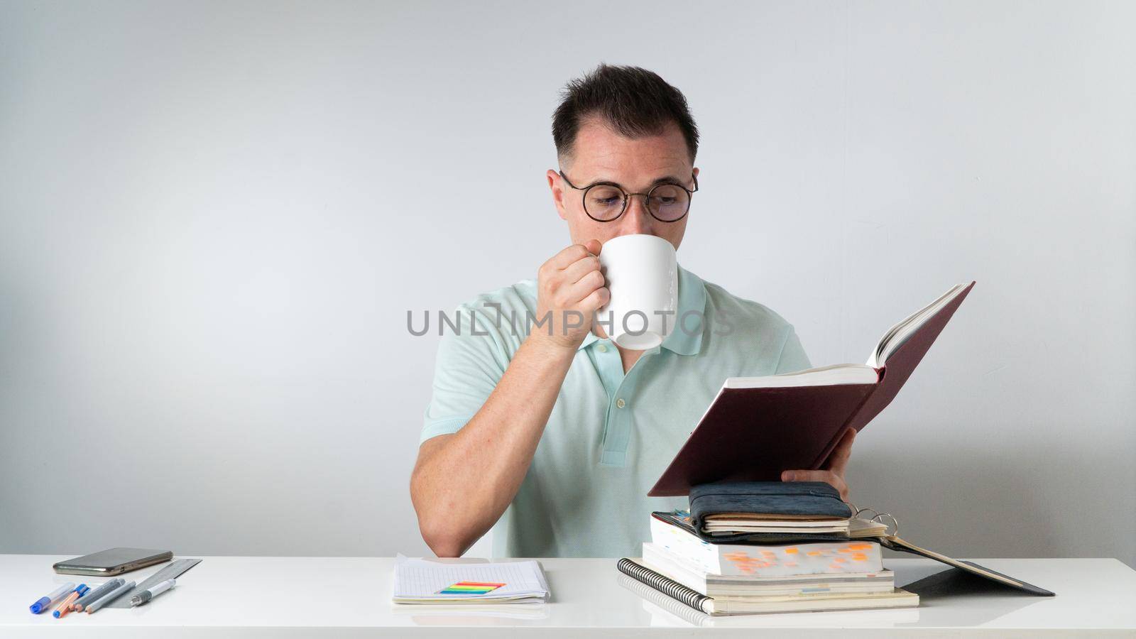A student guy reading a book and drinking coffee at his desk - studying. High quality photo