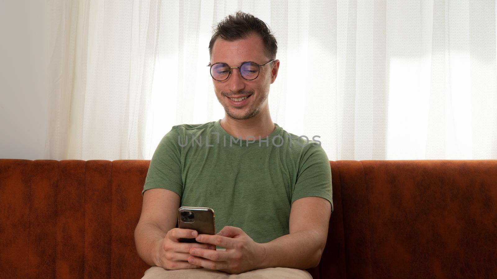 A satisfied man chats in a smartphone from home on the couch. High quality photo