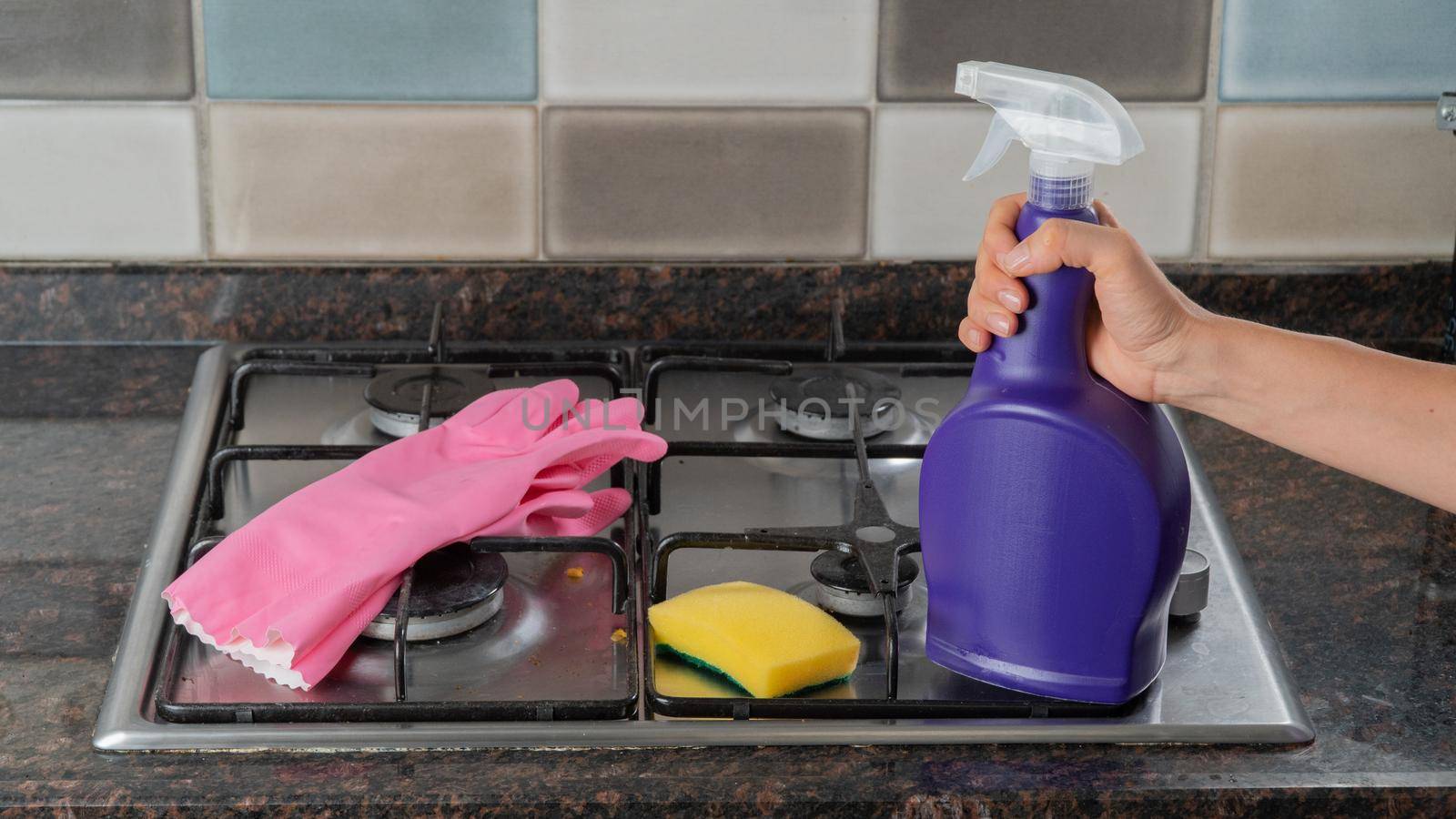 Rubber gloves, sponge and hand holding detergent on the gas stove - cleaning and washing kit