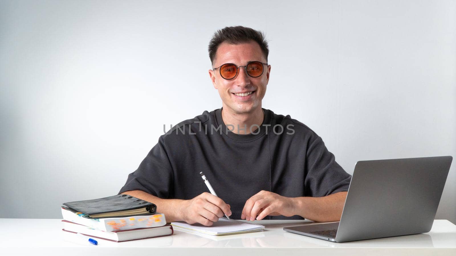 A cheerful student learns with books, notebooks and a laptop at his desk by voktybre