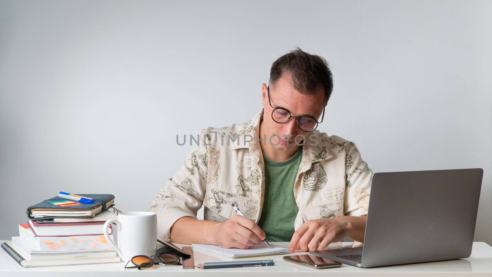 A student at a table with textbooks and notebooks writes in a notebook. High quality photo