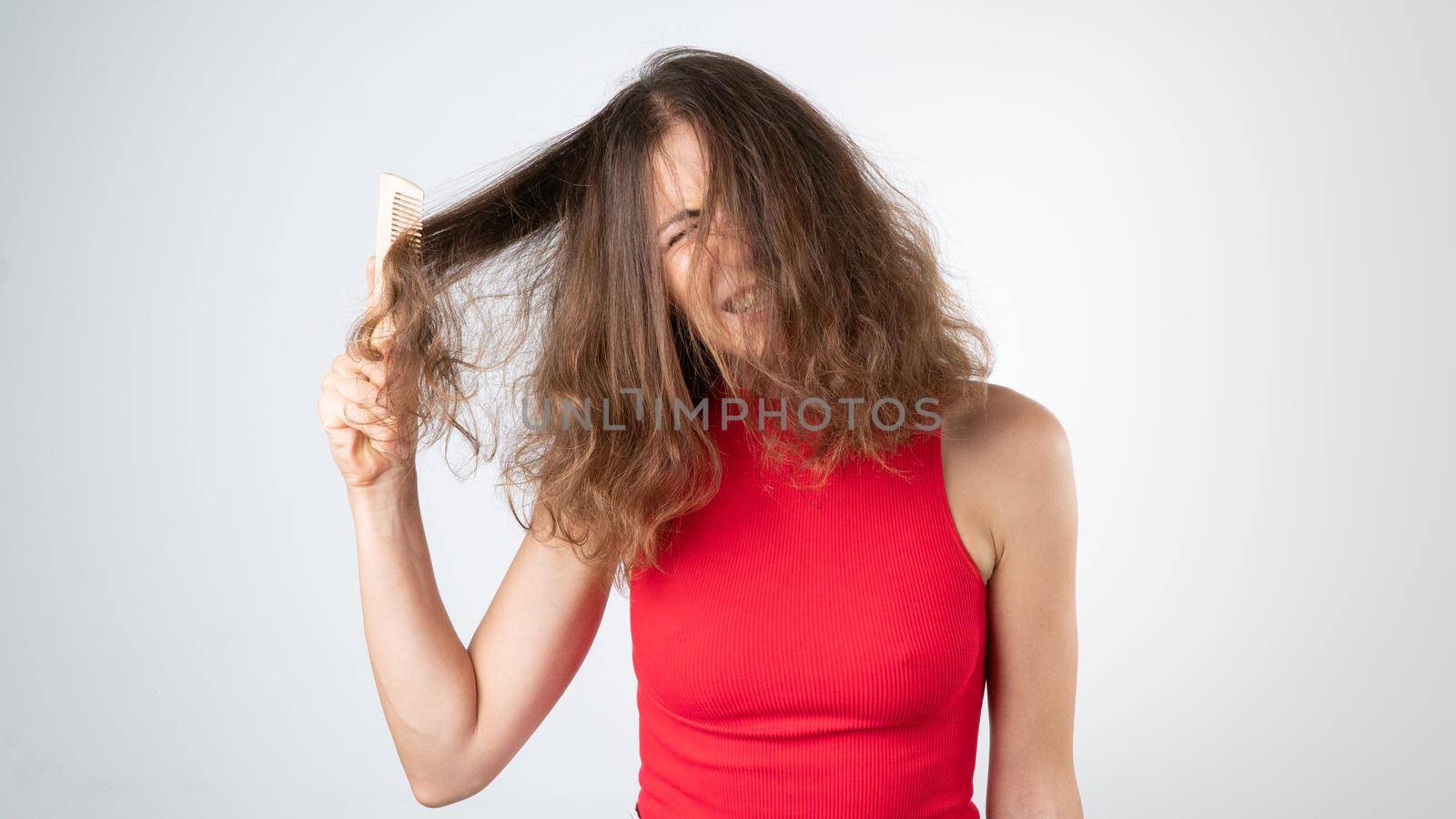 A woman's grimace when it hurts, a complex combing of unruly tangled hair with a comb by voktybre